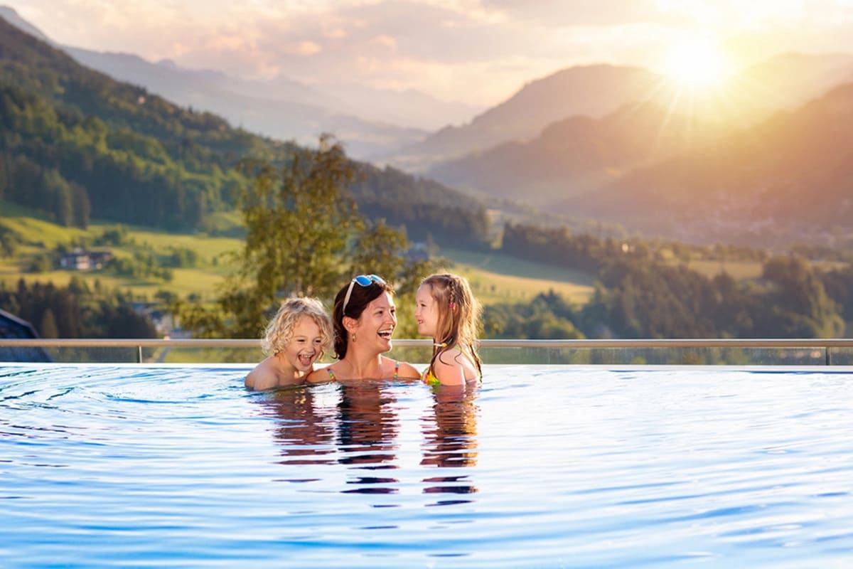 Mama cu doi copii bucurandu-se de piscina unui resort cu vedere spre munti